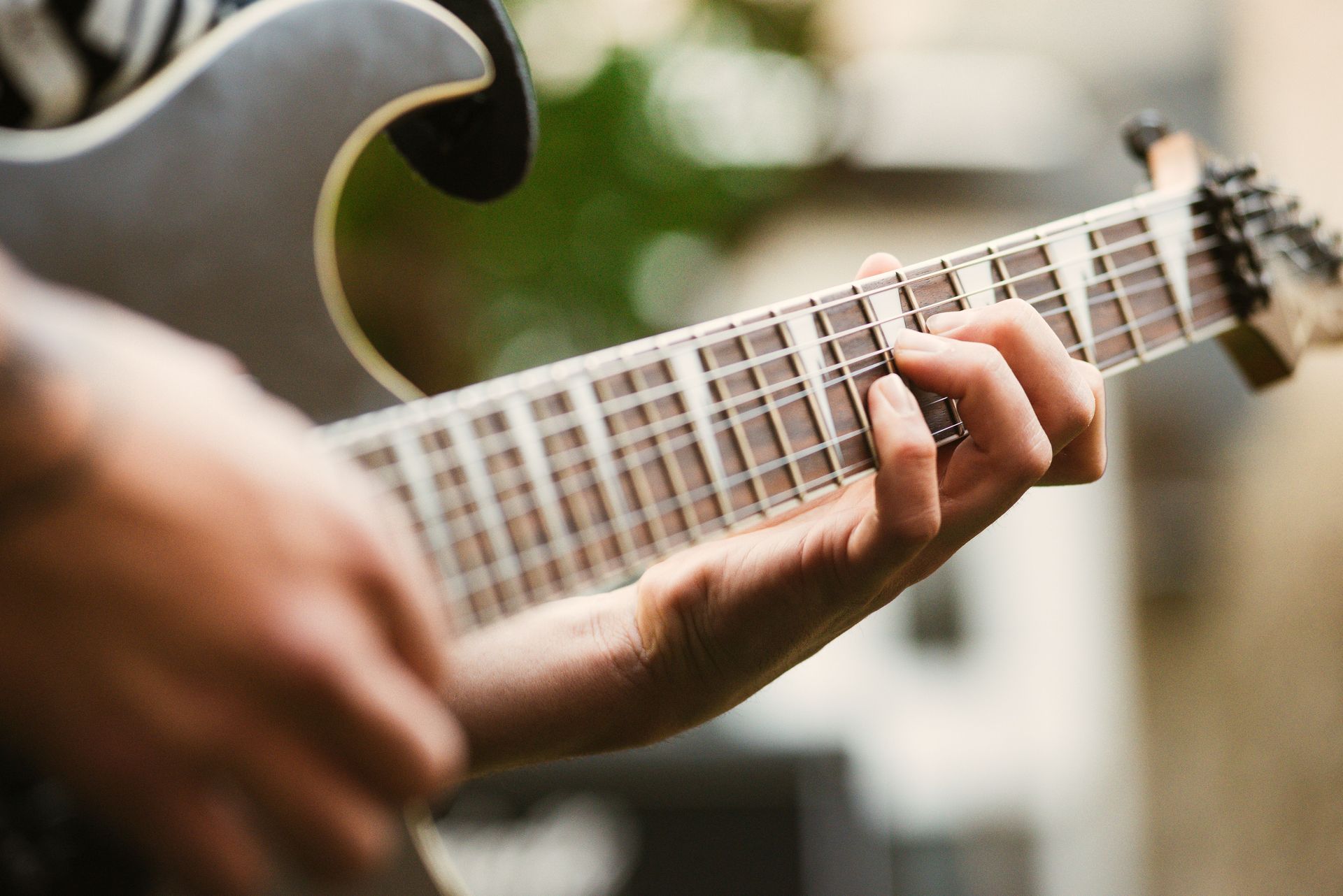 Detailed shot of a guitarist's hand playing an electric guitar outdoors.
